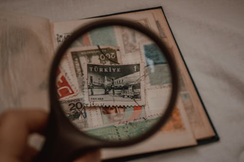 Close-up of Person Holding a Magnifying Glass over Post Stamps 
