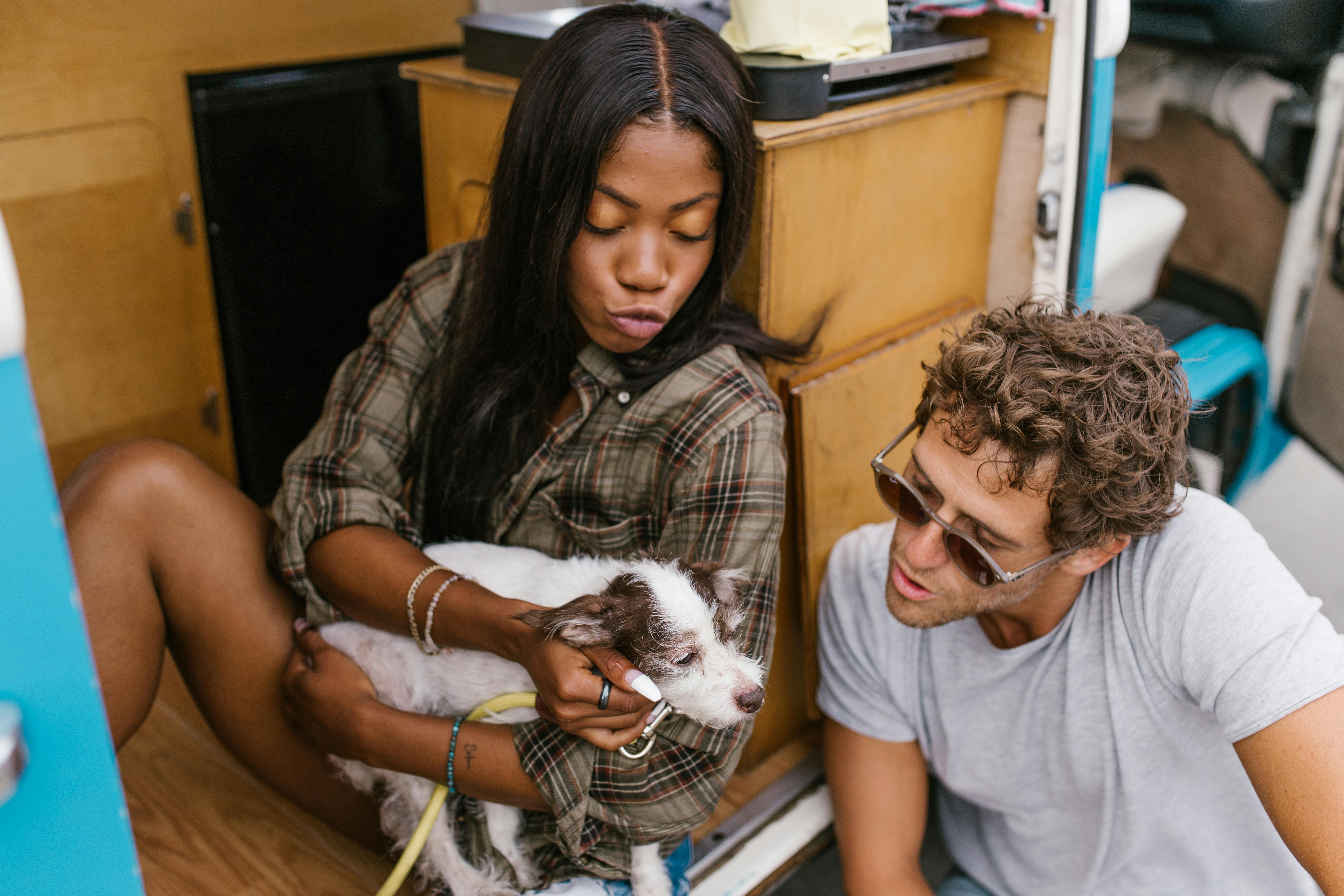 A young couple sits inside a campervan, lovingly interacting with their pet dog during a travel adventure.