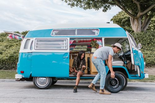 Free A couple enjoying a road trip, fixing a tire on their vintage Volkswagen van parked outdoors. Stock Photo