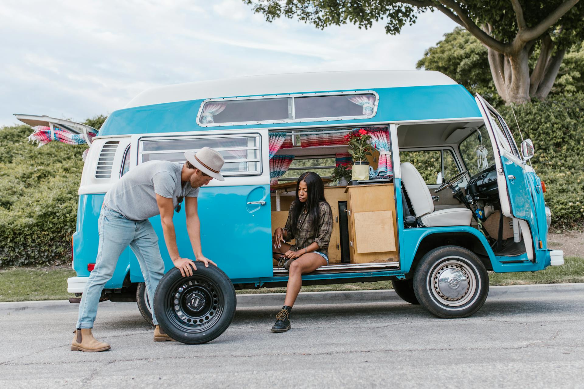 Man and woman enjoying a road trip with their camper van, preparing a spare tire.
