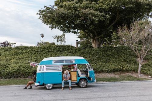 Free A couple enjoying a sunny day next to a retro blue camper van parked by greenery. Stock Photo