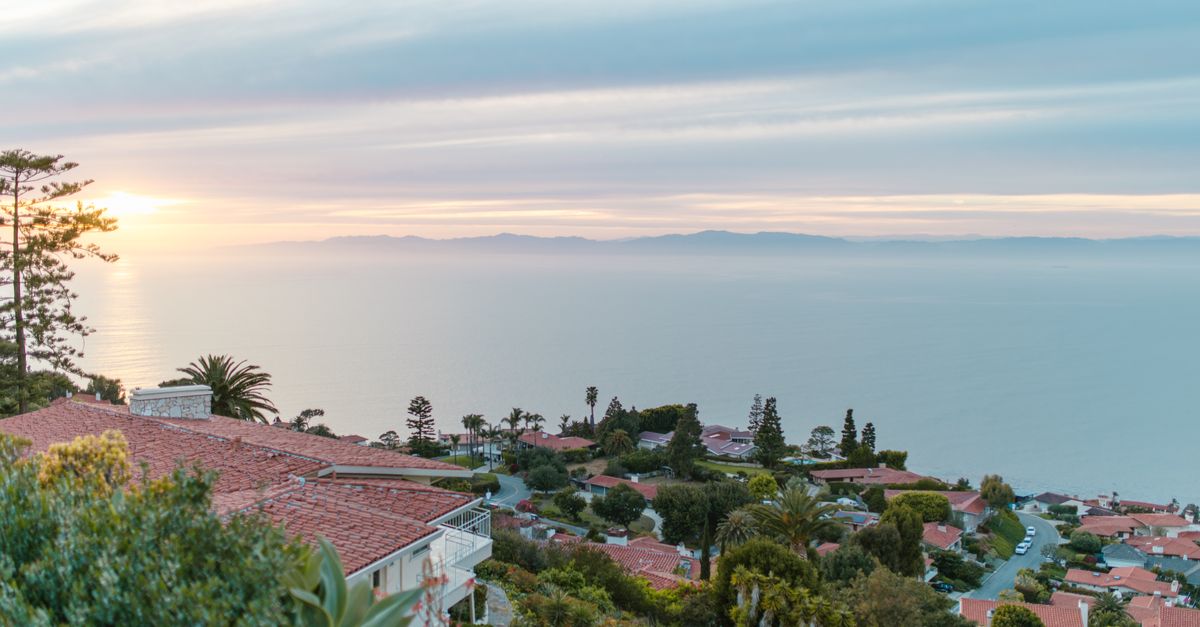 Serene view of a coastal town with red rooftops overlooking the ocean at sunrise, offering a tranquil ambiance.