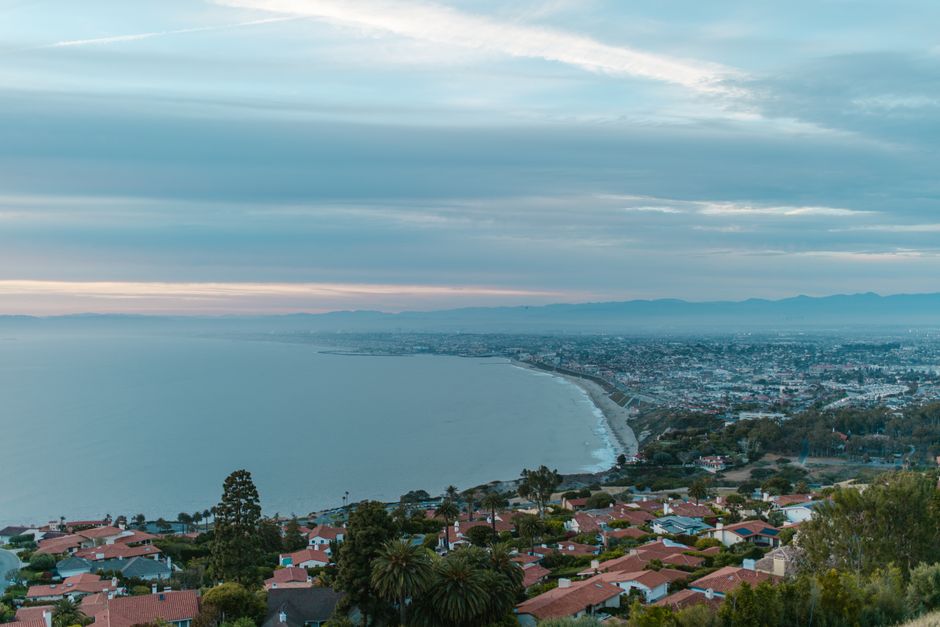 Aerial view of a coastal city at twilight with shoreline and cityscape.