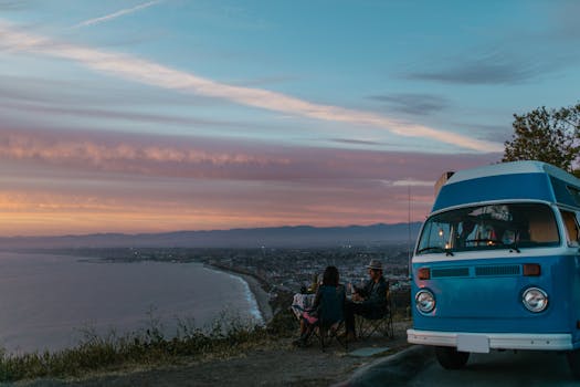 A vintage camper van parked by the seashore with people enjoying a sunset view. Ideal for travel themes.
