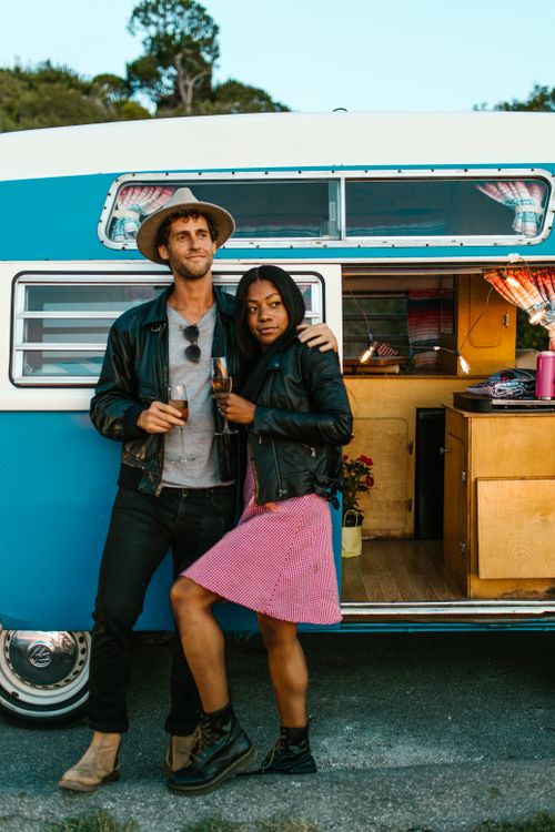 Free Young couple standing by campervan, enjoying their trip in summer with drinks. Stock Photo