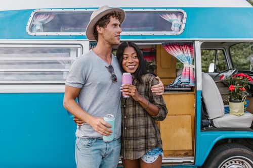 Free Smiling couple enjoying drinks by a blue camper van. Outdoor adventure vibes. Stock Photo