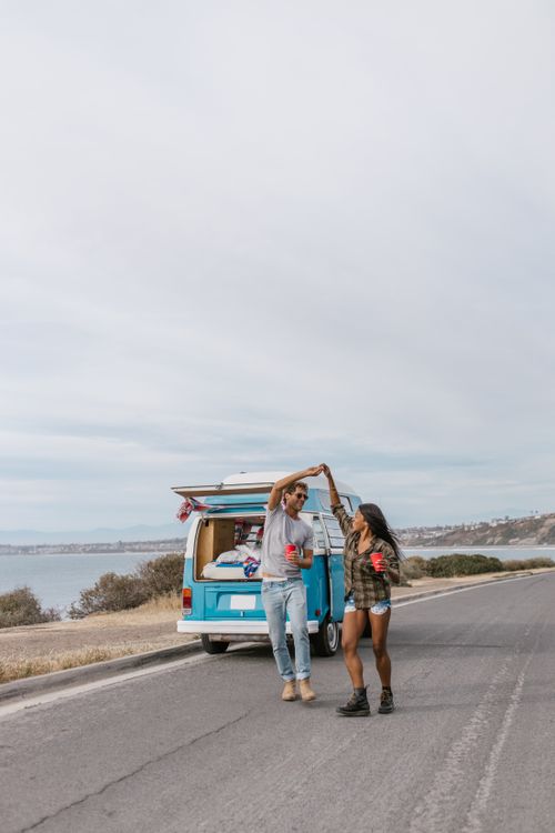 Free A joyful couple dances by their camper van during a scenic road trip. Stock Photo