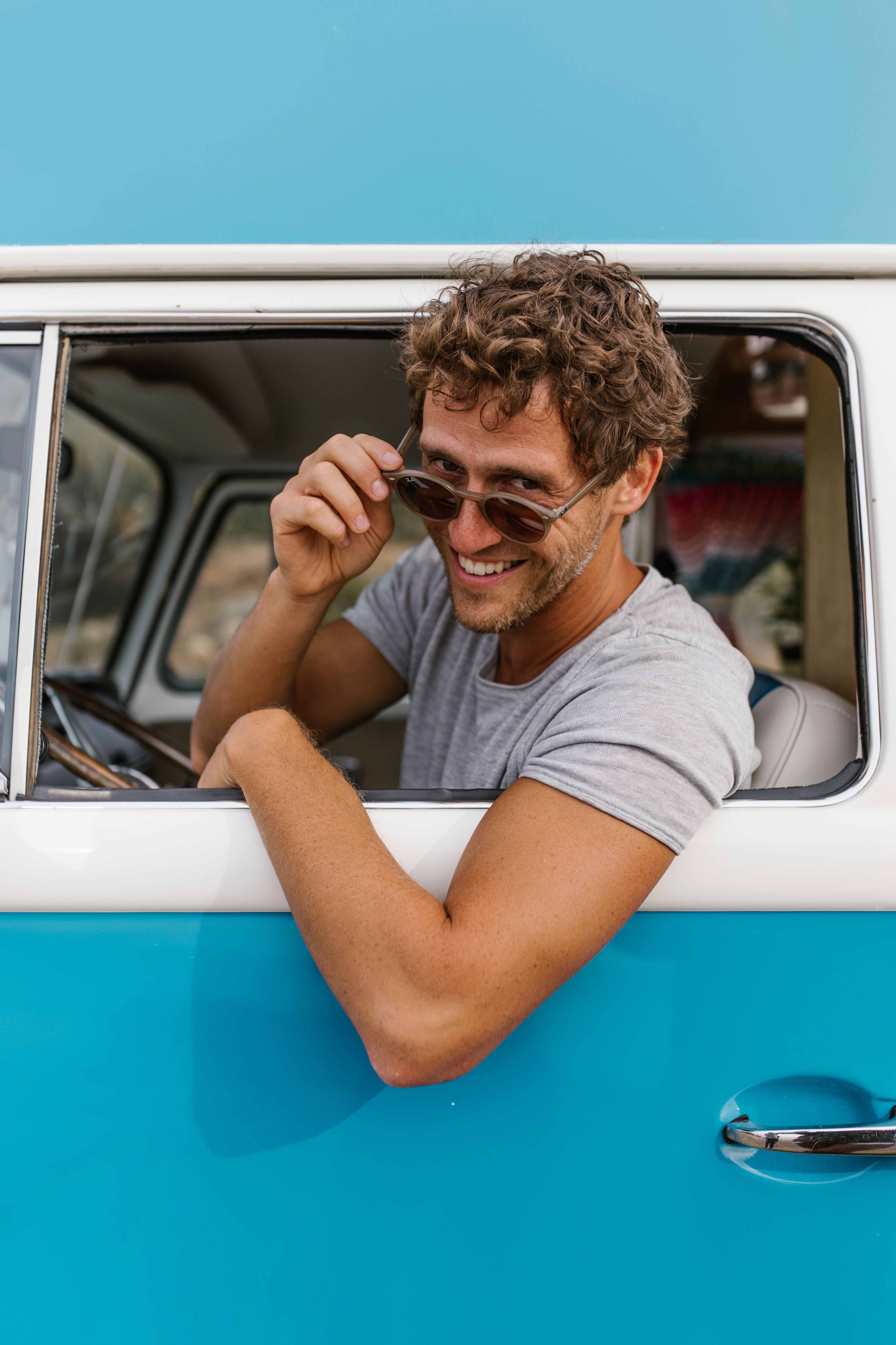 Cheerful man in a blue and white van adjusting sunglasses and smiling.