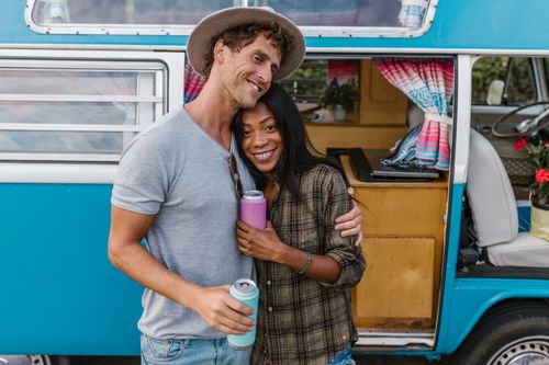 Free Happy couple smiling together by a vintage camper van on a sunny day. Stock Photo