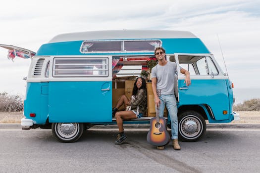 Happy couple enjoying a sunny day by their classic blue camper van with a guitar.