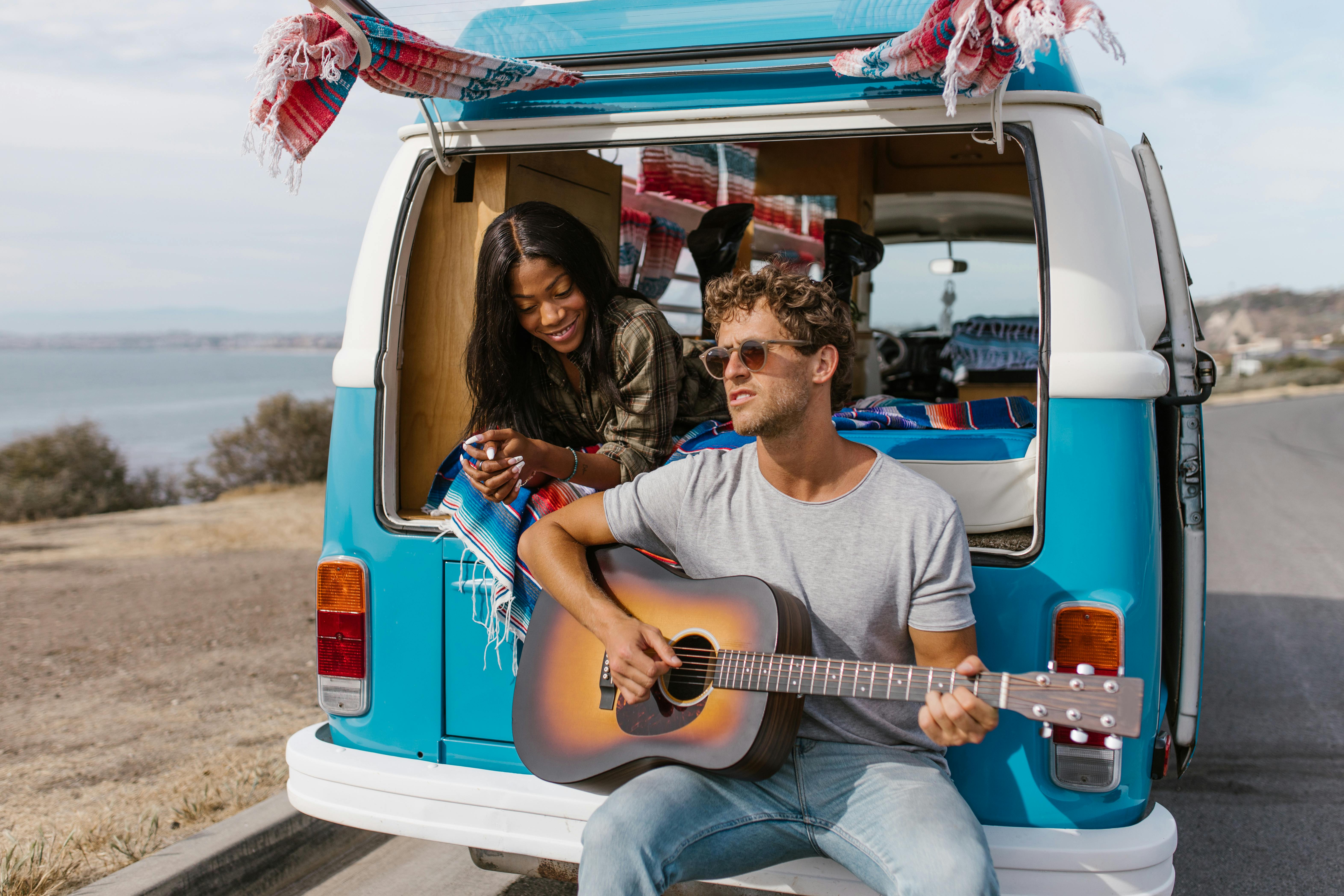 a woman lying in the van watching a man play the guitar