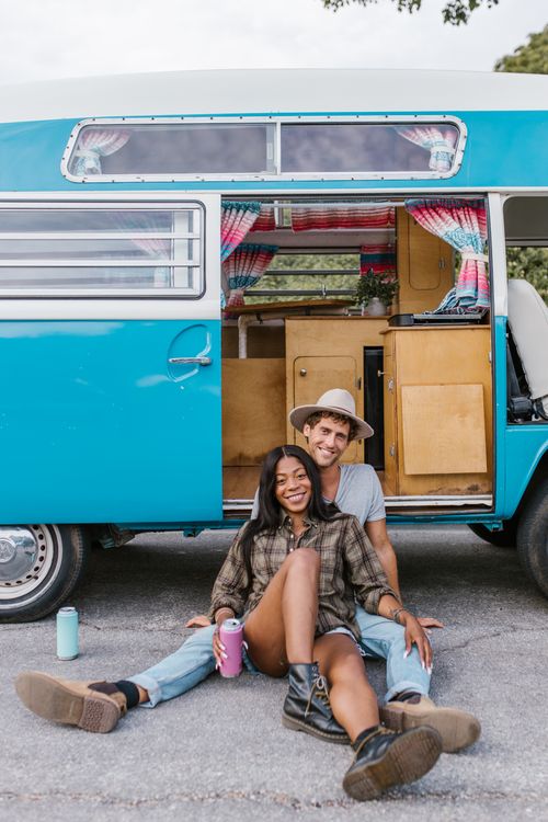 Free Happy couple sitting by classic van enjoying a sunny day outdoors. Embrace the van life spirit. Stock Photo