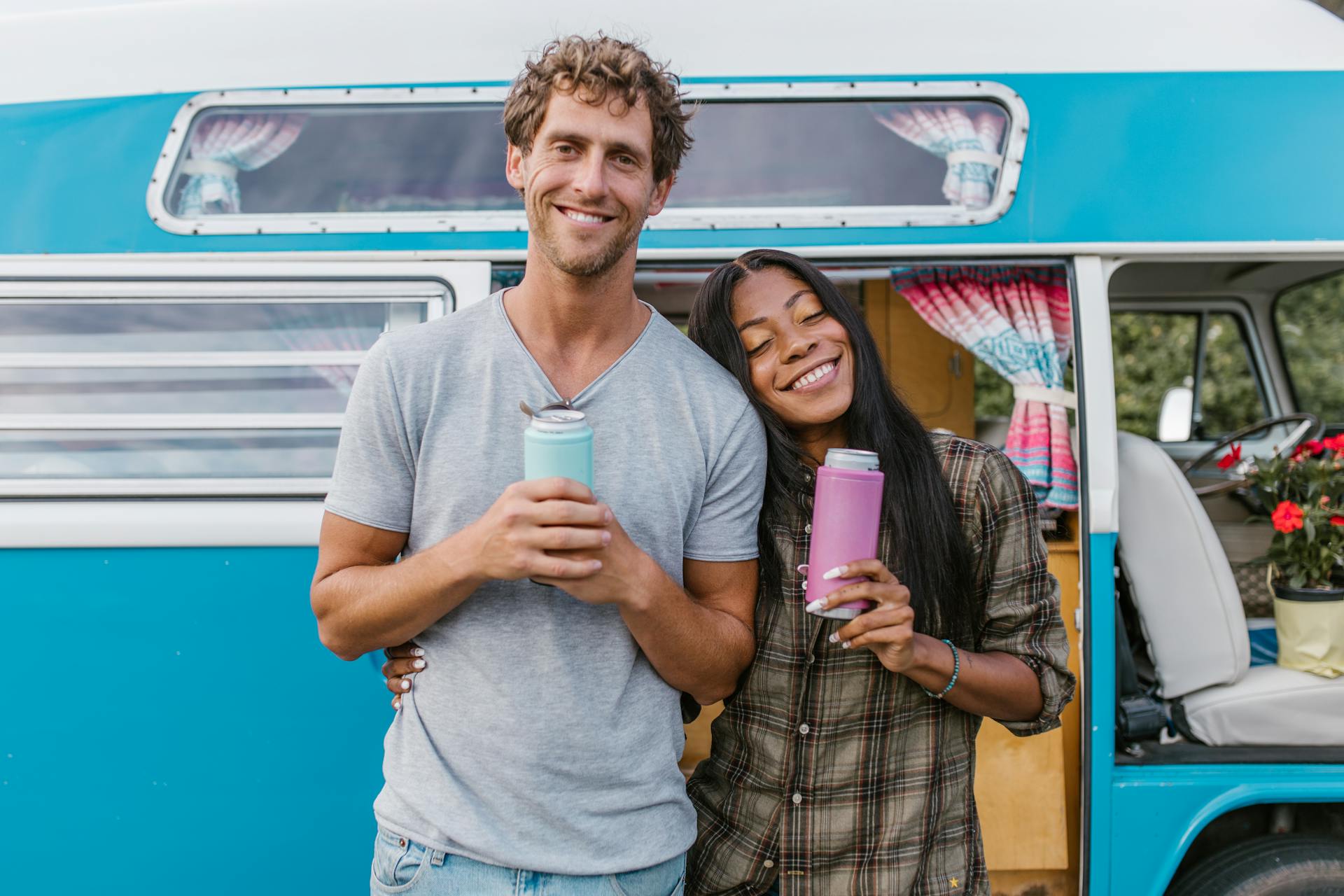 Smiling couple standing by a blue camper van, enjoying their travel adventure.