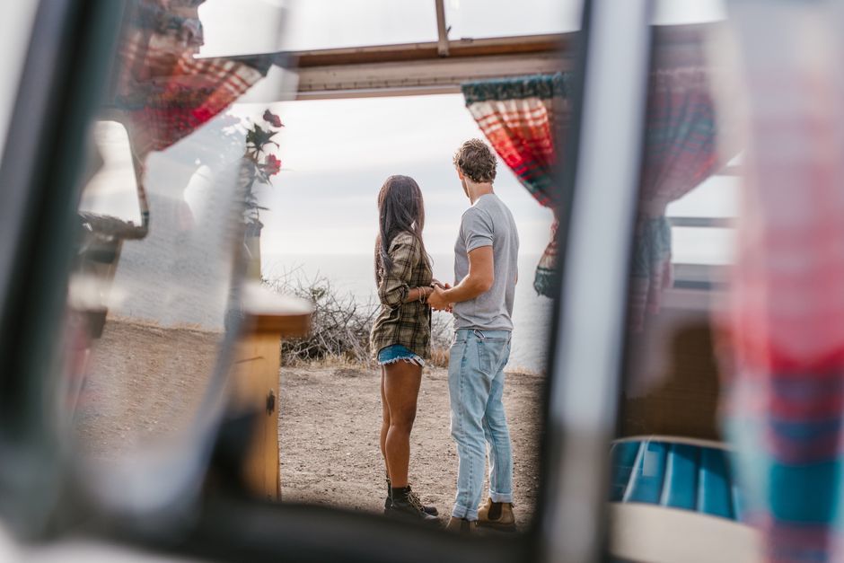 A couple standing by their camper, holding hands, enjoying the ocean view.