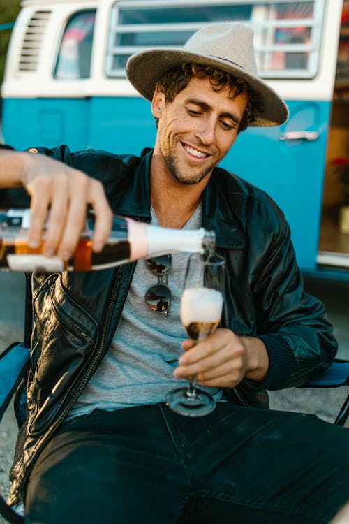 Man Sitting near a Campervan and Pouring Champagne into a Glass