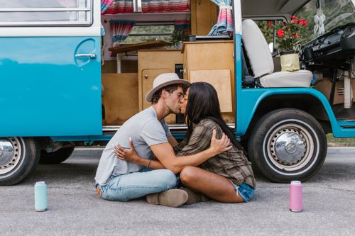 Free Young couple sitting and kissing by a camper van during a road trip. Stock Photo