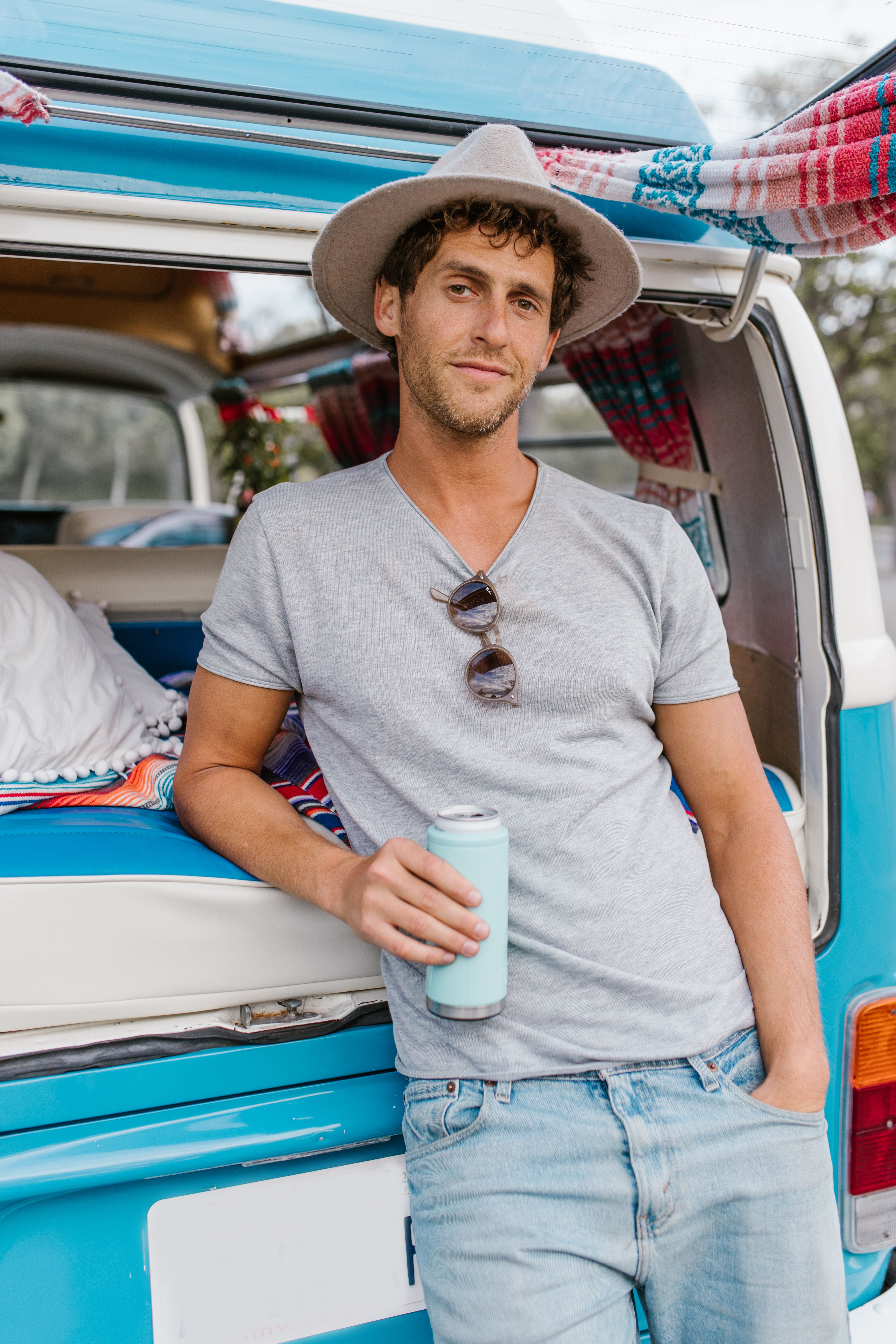 Man in a hat holding a can, leaning on a camper van. Outdoor travel vibe.