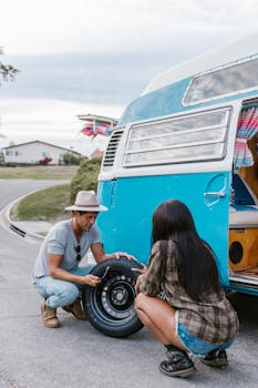 Young couple fixing a flat tire on a vintage blue camper van. Perfect for content on road trips, adventure, and outdoor lifestyle.