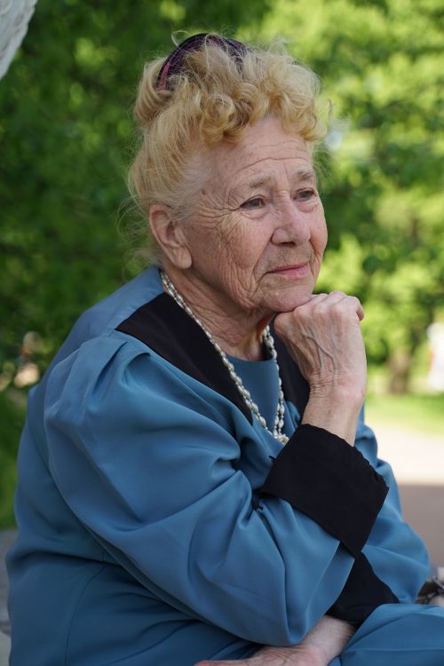 Free Elderly woman with thoughtful expression sitting outdoors in St. Petersburg, wearing a blue blouse and pearls. Stock Photo