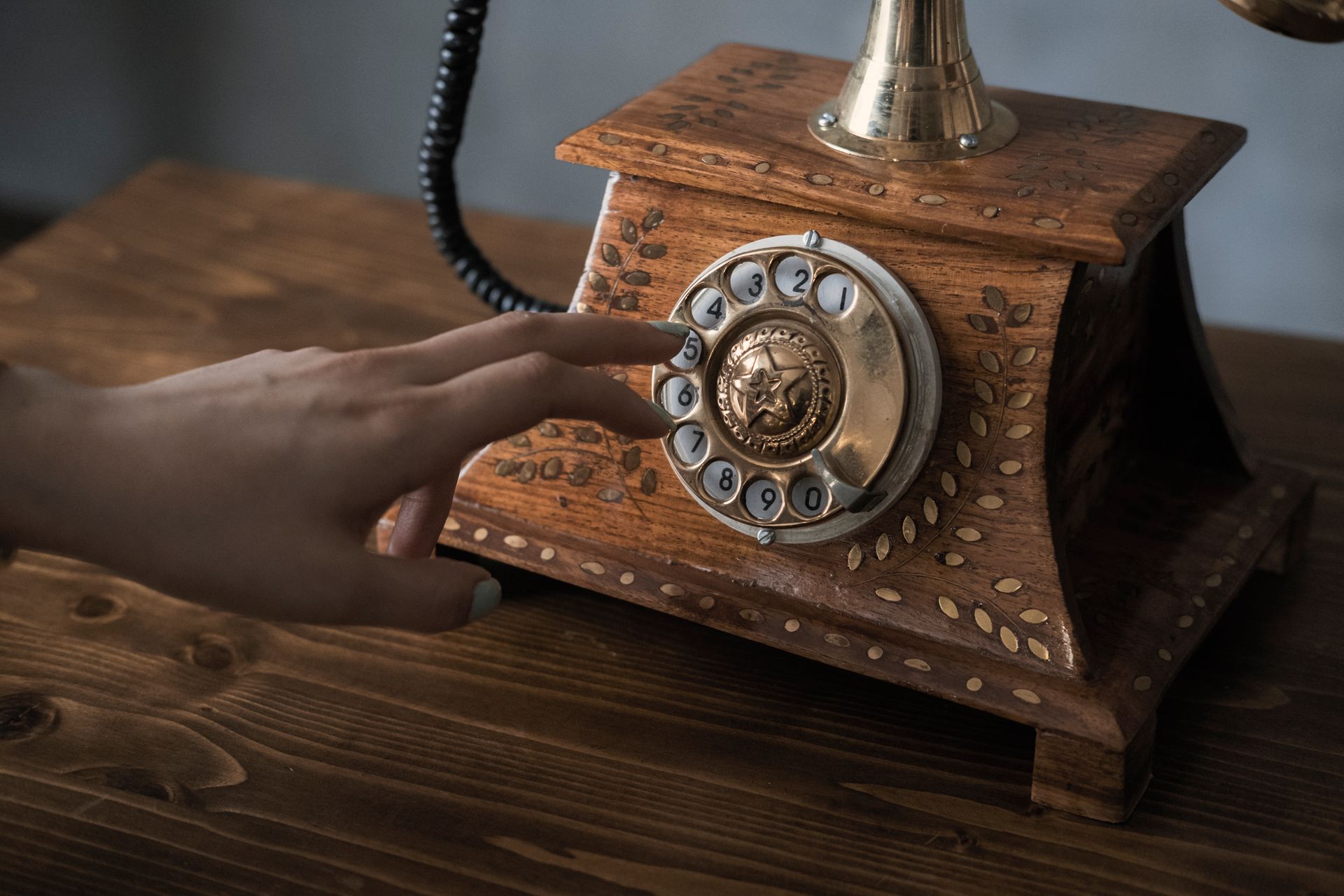 A close-up of a hand dialing a vintage wooden rotary telephone indoors.