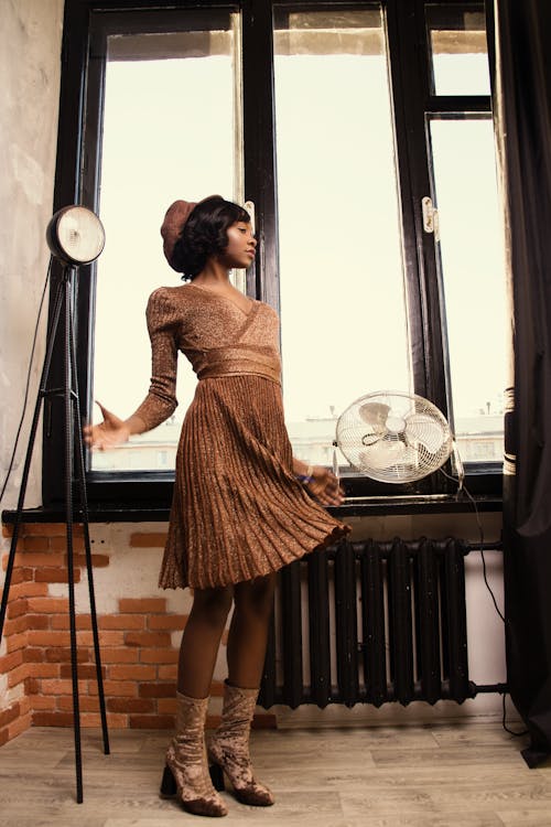бесплатная Женщина в коричневом платье стоит у черного стола Стоковое фото
