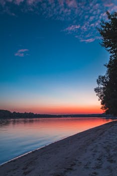 Peaceful sunrise over a serene lakeside with calm water and vibrant sky colors.