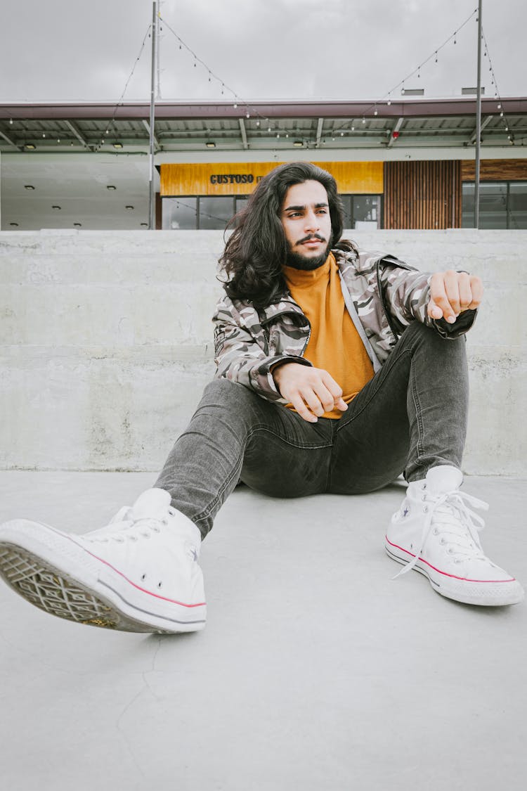 Young Man With Long Hair And Beard Sitting In City 