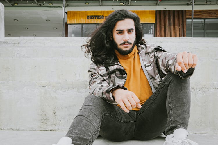 Young Man With Long Hair And Beard Sitting Outdoors 