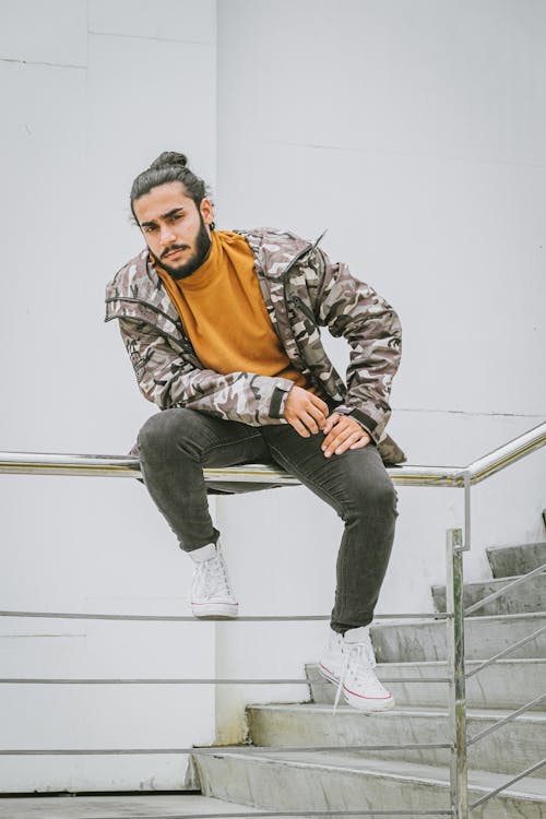 A Man Sitting on the Stainless Steel Railings Near the Concrete Wall and Stairs