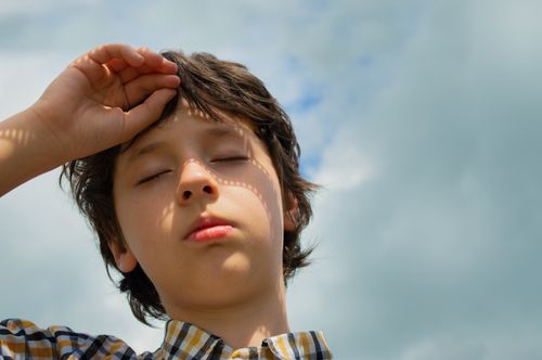 Free Close-up portrait of a young boy with eyes closed, hand on head under a clear sky. Stock Photo