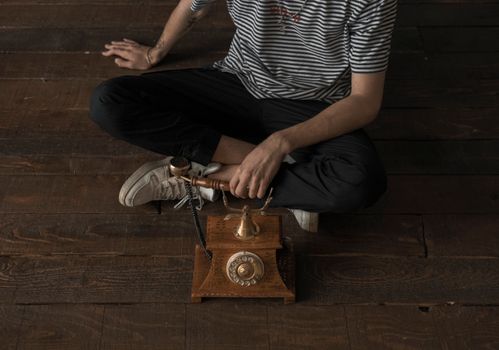 Person sitting on wooden floor with vintage phone, wearing striped shirt.