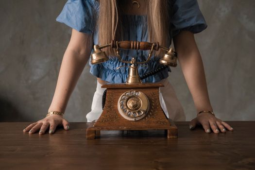 A young woman leans over a vintage rotary phone on a wooden table, evoking nostalgia.