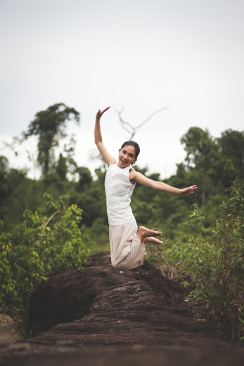A Woman in White Close Jumping on the Rock Formation