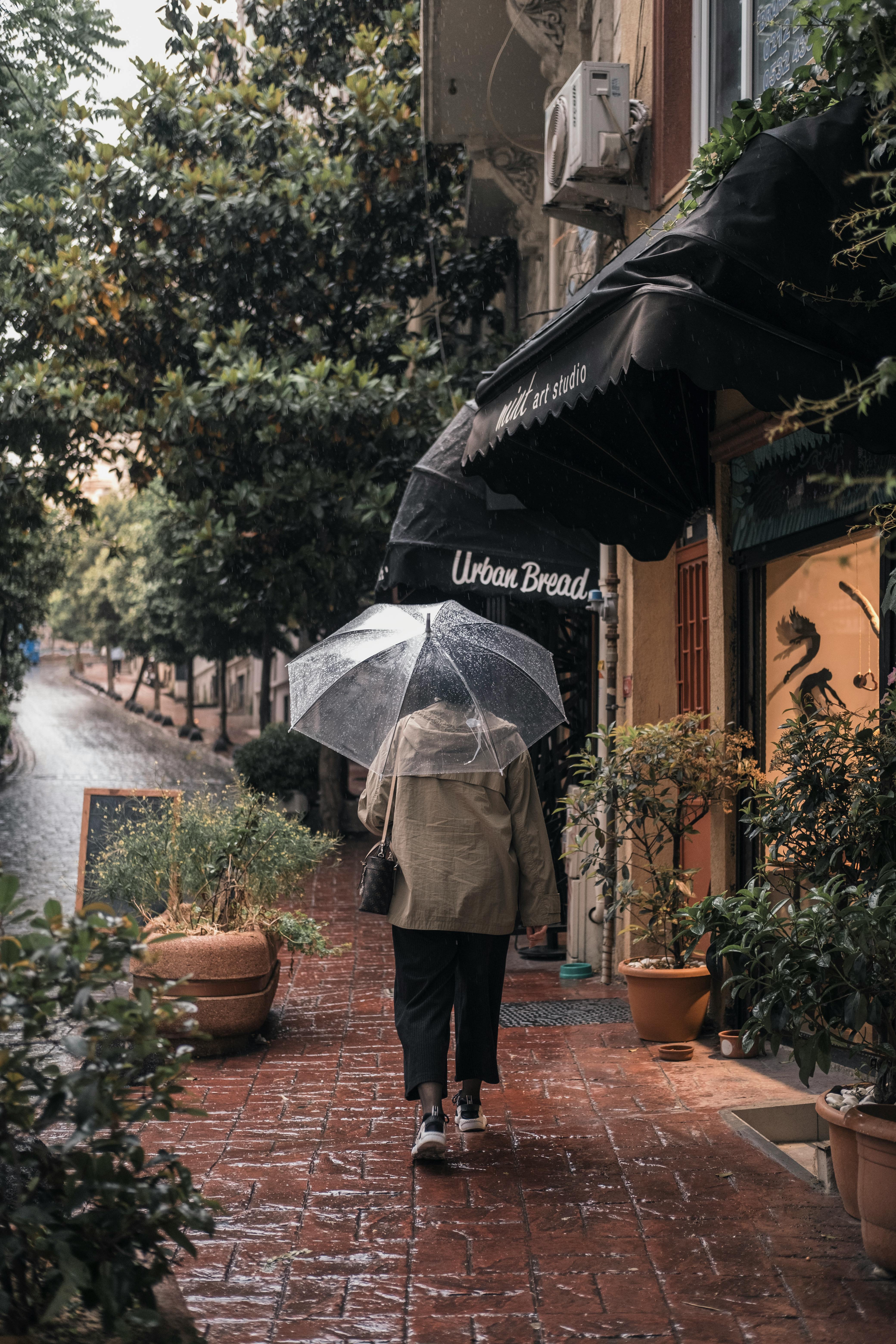 A woman walks on a rainy city street, captured in a moody and atmospheric scene with an umbrella.