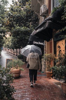 A woman walks on a rainy city street, captured in a moody and atmospheric scene with an umbrella.