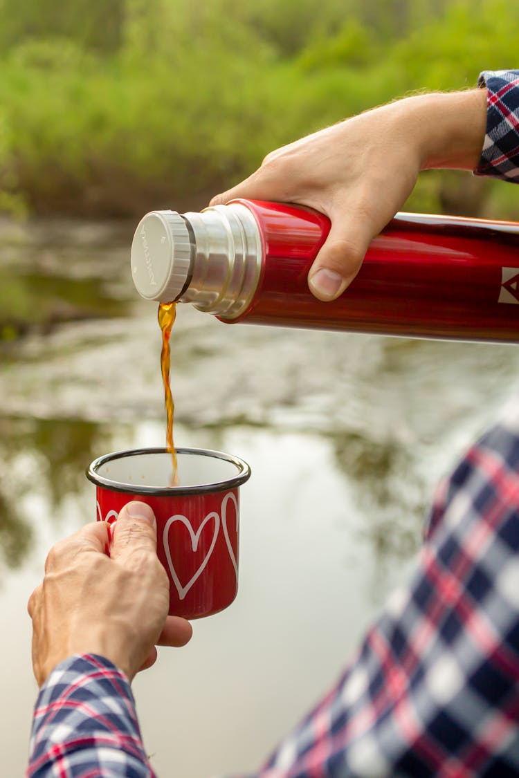 A Person Pouring Coffee Into The Cup From The Thermos