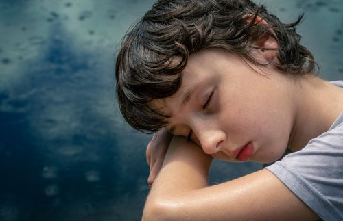 Free Close-up of a young boy resting peacefully outdoors by a serene water surface during the day. Stock Photo