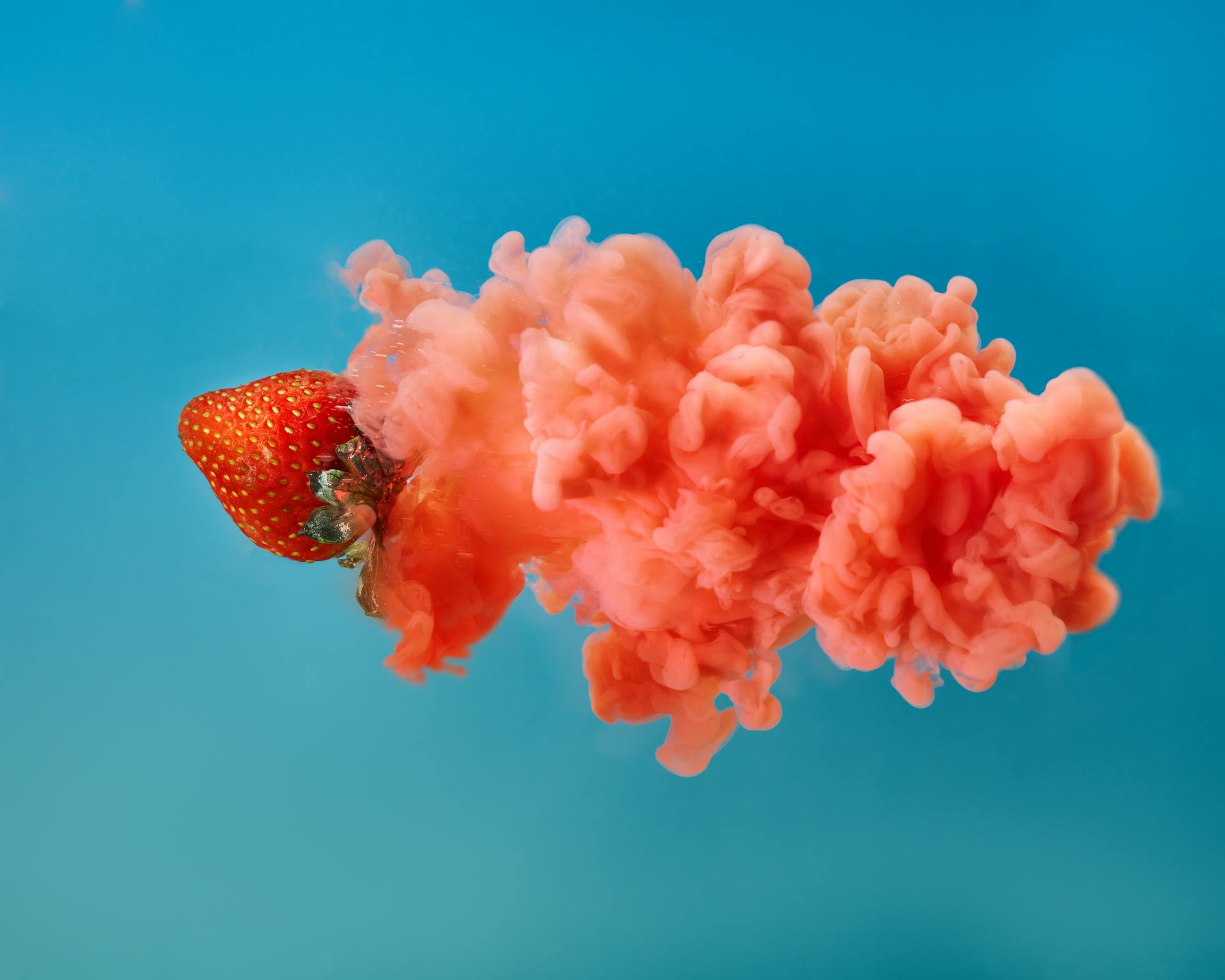 Close-up of a strawberry with colorful smoke against a blue background, creating a dynamic visual effect.