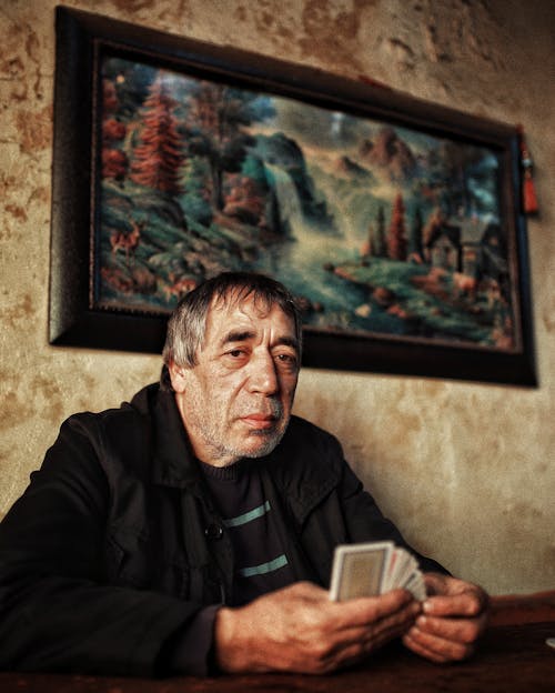 A Man Holding Playing Cards Sitting Near the Picture Frame