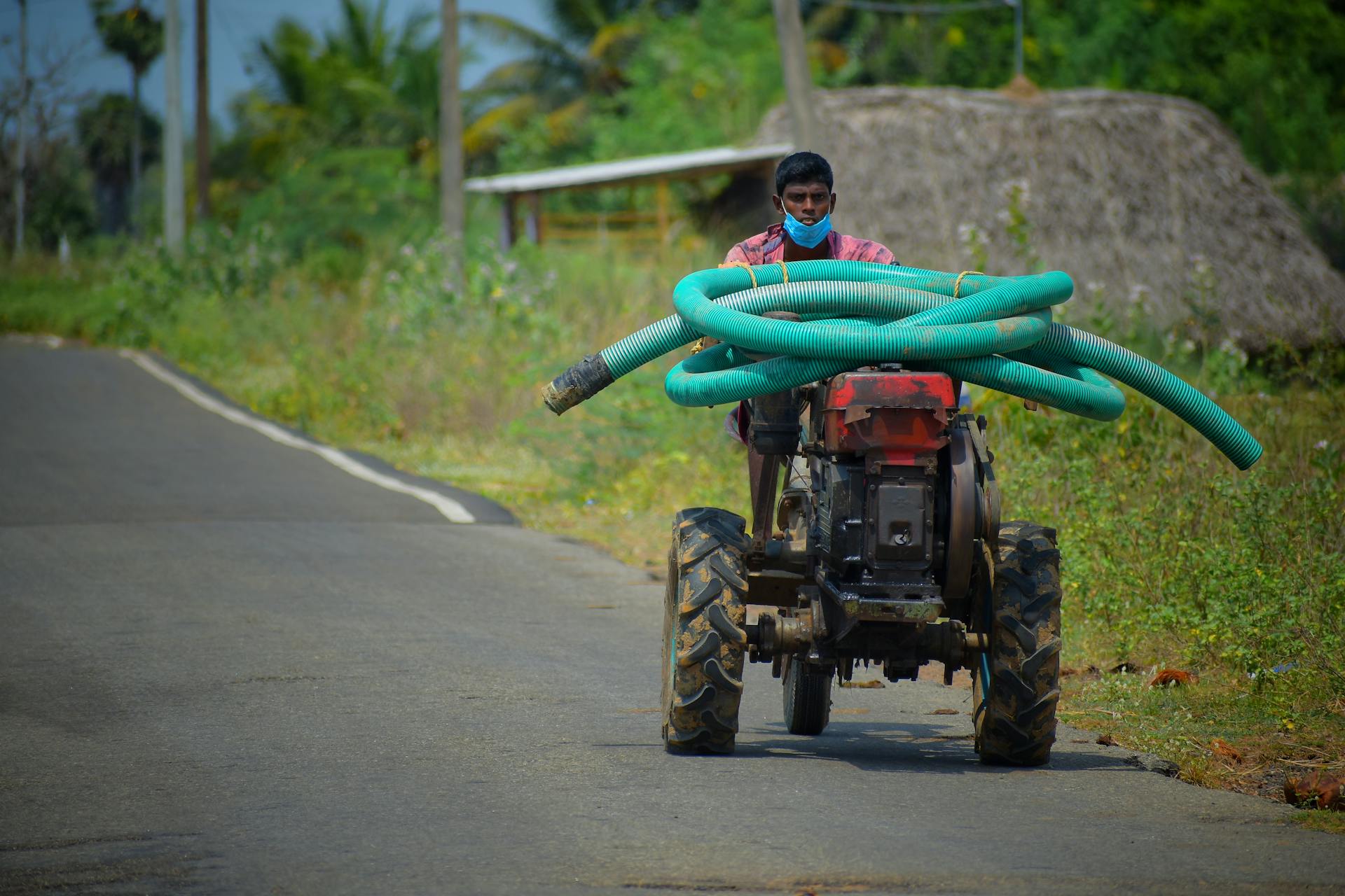A farmer drives a tractor carrying hoses on a rural road in Peravurani, India. Captured during the day.
