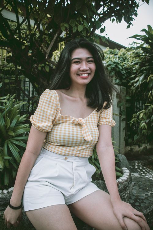 Free Cheerful woman in a yellow gingham top posing outdoors surrounded by greenery. Stock Photo