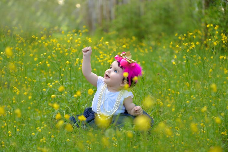 Little Baby Girl Sitting On Grass Among Yellow Flowers 