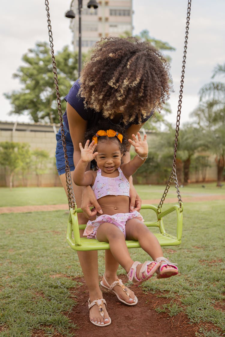 Unrecognizable Mother With Smiling Black Daughter On Swing In Park