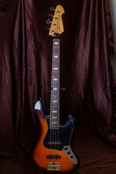 Vertical shot of a classic electric bass guitar against a brown fabric backdrop, ideal for music themes.