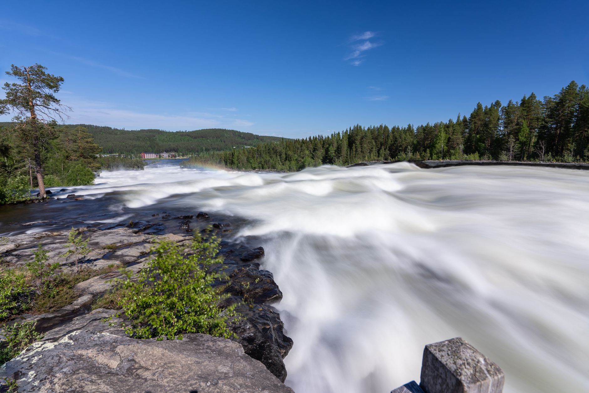 Captivating view of Älvsbyn waterfall in Sweden, surrounded by lush forests under a clear blue sky.