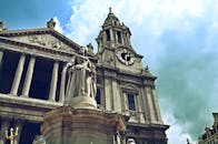 在阴云密布的天空下，低角度拍摄了伦敦圣保罗大教堂和安妮女王雕像