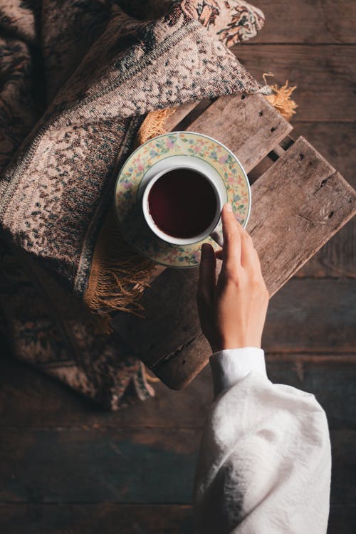 Crop person taking tea mug from chair covered with carpet