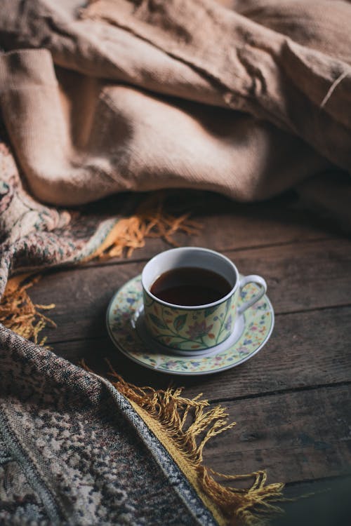 Free From above of cup of hot tea and saucer placed on wooden floor against carpet pushed back Stock Photo