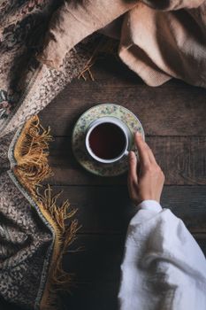 Crop person with cup of tea on floor near carpet