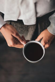 A person holds a ceramic cup filled with coffee, captured from above with warm tones.